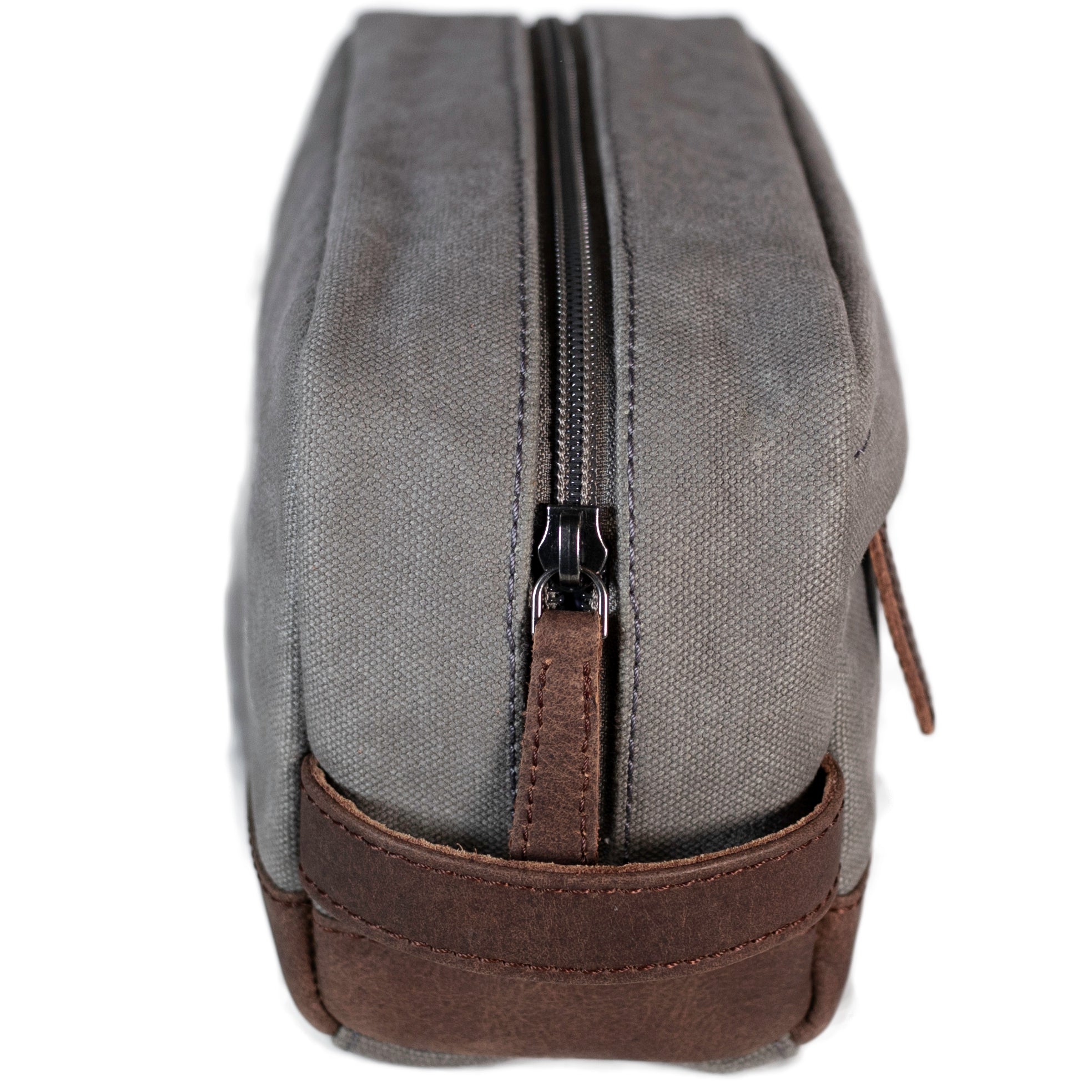 A grey canvas toiletry bag and brown leather details, featuring a zipper closure and a brand logo embossed on the front.